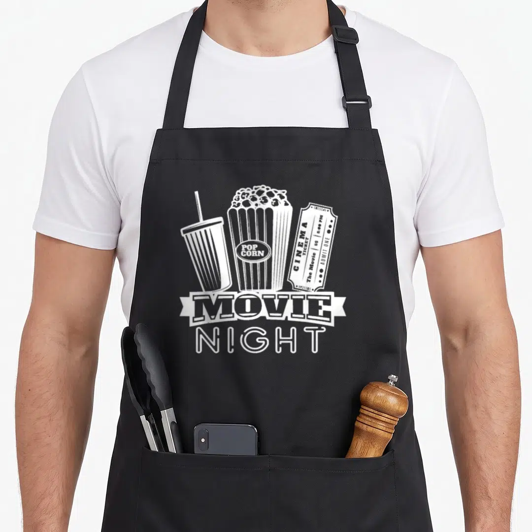 Candy family aprons - White line art of soda, popcorn, and cinema ticket reading MOVIE NIGHT — shown on a black cotton canvas apron against a white background