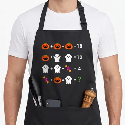 Operation halloween apron - Math equations with orange pumpkins, white ghosts, purple candy, and green question mark — shown on a black cotton canvas apron against a white background
