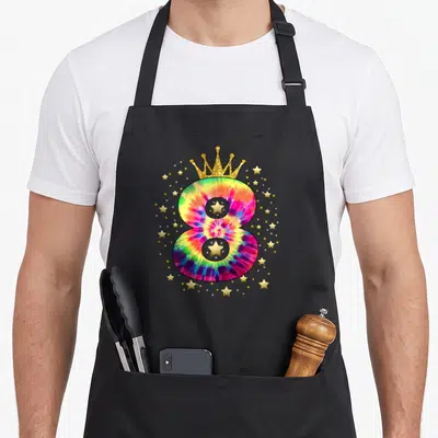 Colorful tie apron - Tie-dye number 8 with gold crown and scattered gold stars on black fabric — shown on a black cotton canvas apron against a white background
