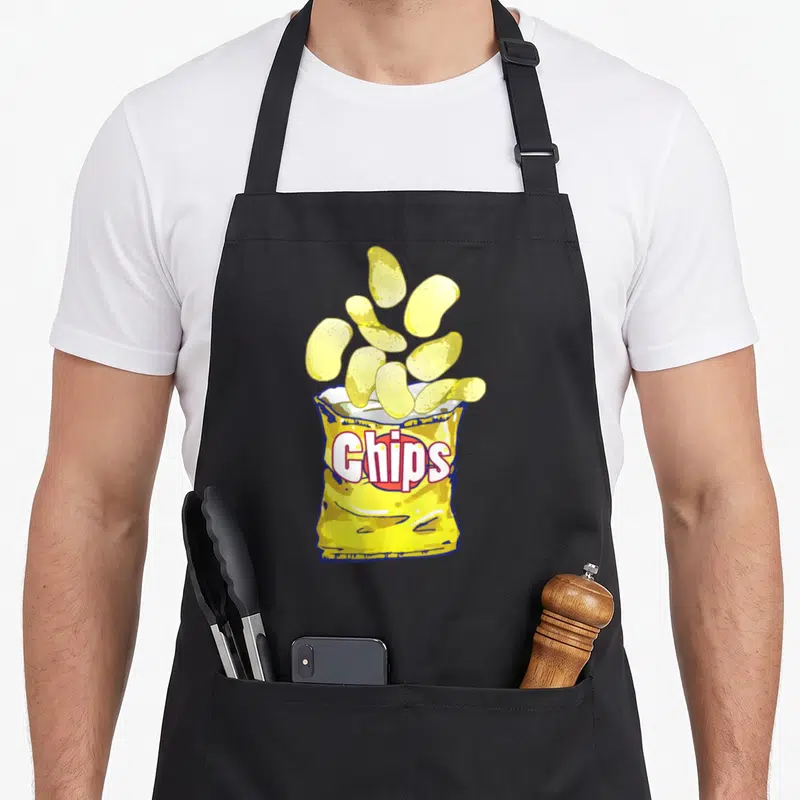 Game potato apron - Cartoon yellow bag of chips with floating crisps and red outlined text — shown on a black cotton canvas apron against a white background