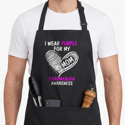 Cute fibromyalgia awareness apron - White heart with mom text and purple I Wear Purple For My Mom Fibromyalgia — shown on a black cotton canvas apron against a white background