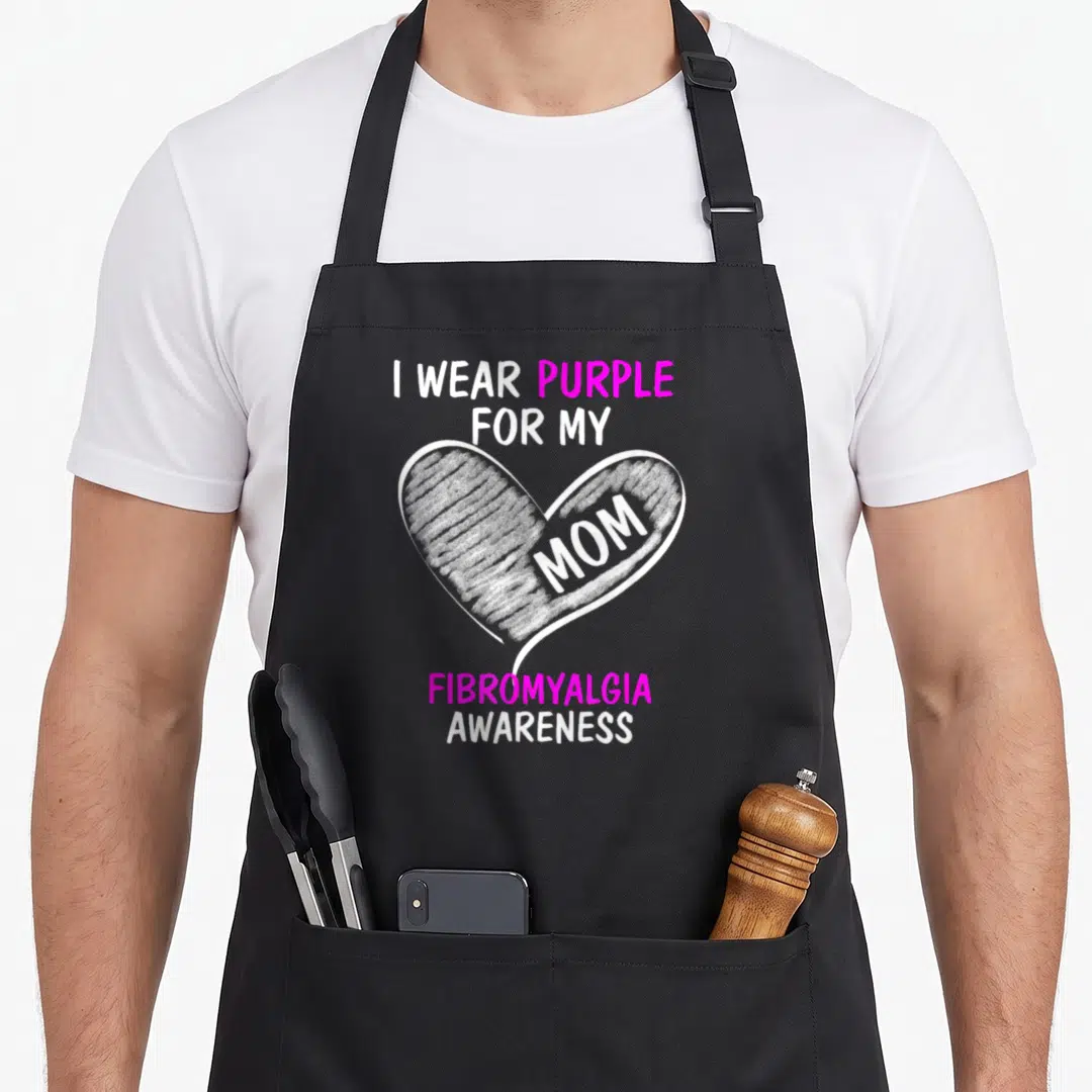 Cute fibromyalgia awareness apron - White heart with mom text and purple I Wear Purple For My Mom Fibromyalgia — shown on a black cotton canvas apron against a white background