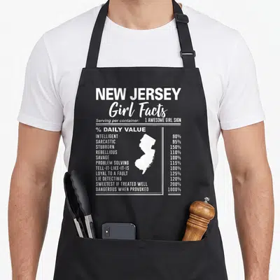 Jersey novelty apron - White New Jersey map silhouette surrounded by sarcastic girl fact percentages in nutrition label — shown on a black cotton canvas apron against a white background