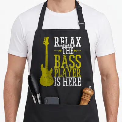 Guitar bass apron - Yellow bass guitar silhouette next to stacked white and yellow distressed text reading RELAX — shown on a black cotton canvas apron against a white background