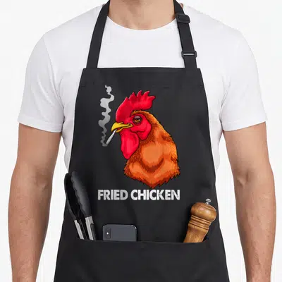 Smoking chicken apron - Cartoon rooster smoking cigarette with FRIED CHICKEN text below — shown on a black cotton canvas apron against a white background