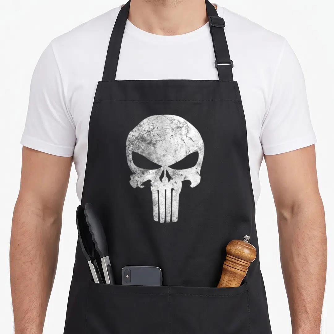 Comic punisher skull apron - White distressed skull graphic with vertical jaw lines on grey background — shown on a black cotton canvas apron against a white background