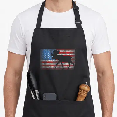 Moose 4th of july apron - Grey moose silhouette standing in front of a weathered red white and blue flag background — shown on a black cotton canvas apron against a white background