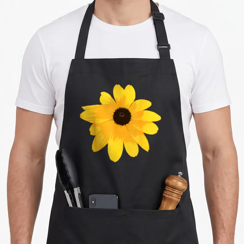 Susan eyed apron - Single yellow flower with brown center photo print — shown on a black cotton canvas apron against a white background