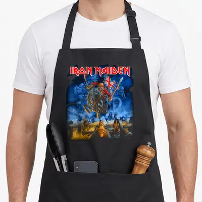 Funny trooper camping apron - Iron Maiden text above Eddie on horse with cannon and skeletons in blue red gold white — shown on a black cotton canvas apron against a white background
