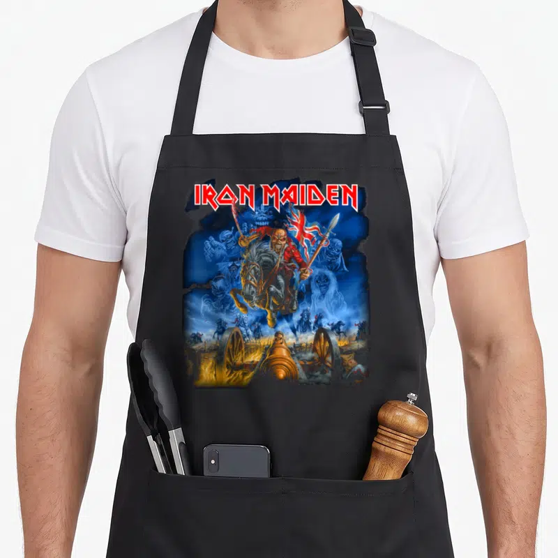 Funny trooper camping apron - Iron Maiden text above Eddie on horse with cannon and skeletons in blue red gold white — shown on a black cotton canvas apron against a white background