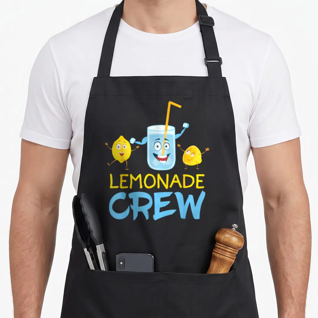 Boss lemonade apron - Cartoon glass of lemonade with arms flanked by two yellow lemons and stacked LEMONADE CREW text — shown on a black cotton canvas apron against a white background