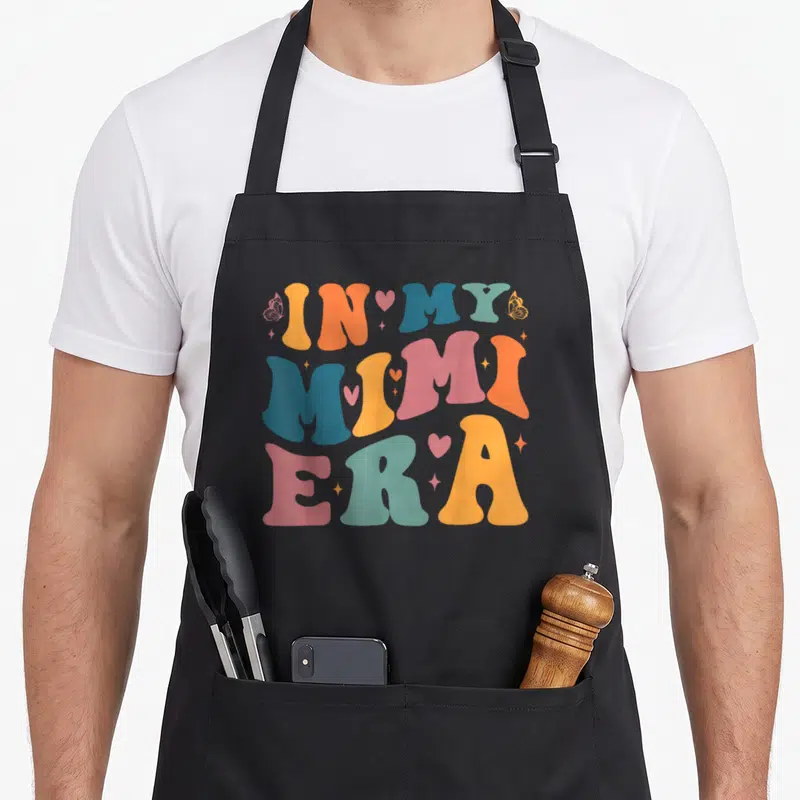 Mimi era mother's day aprons - Retro IN MY MIMI ERA text in orange blue pink with butterflies hearts and stars — shown on a black cotton canvas apron against a white background