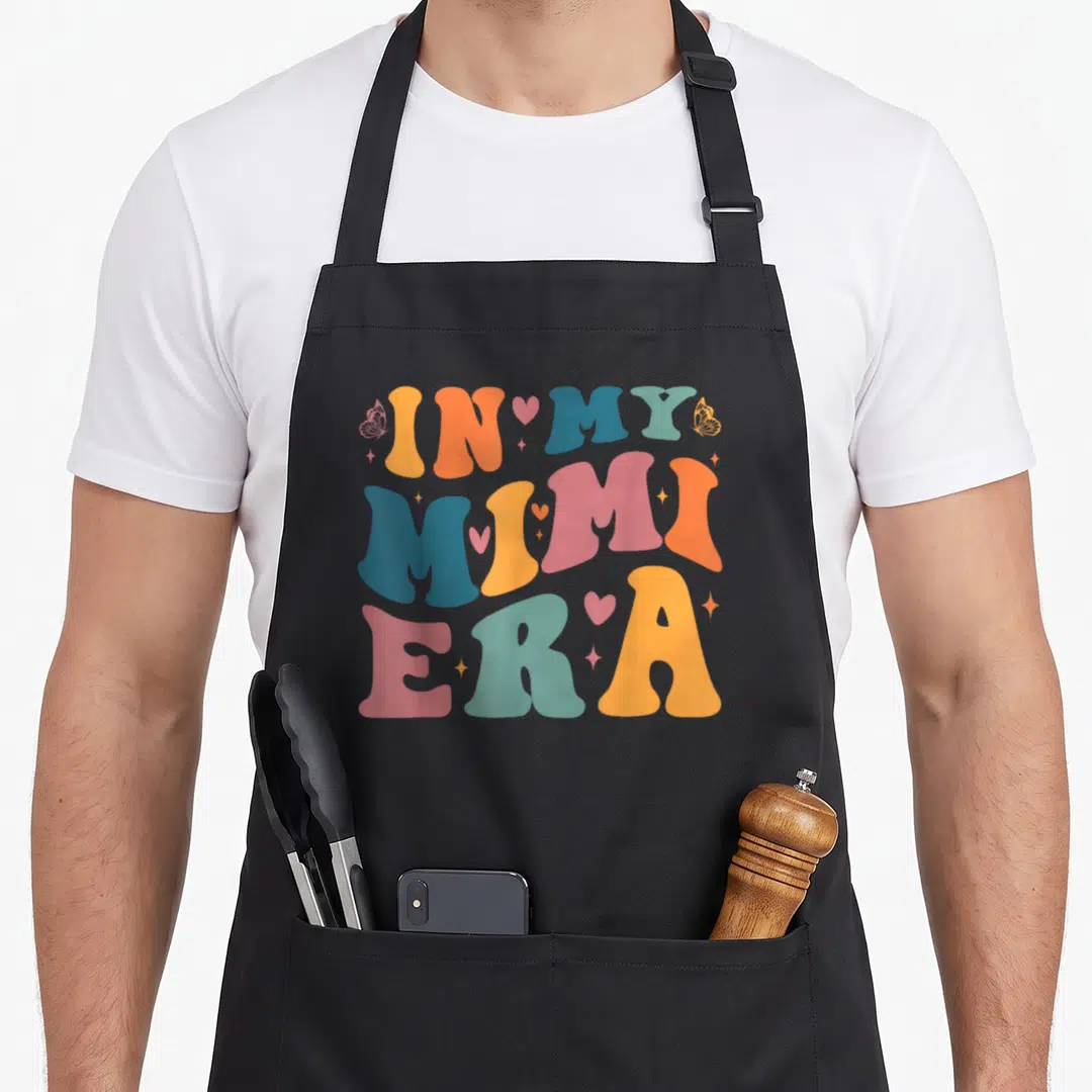 Mimi era mother's day aprons - Retro IN MY MIMI ERA text in orange blue pink with butterflies hearts and stars — shown on a black cotton canvas apron against a white background