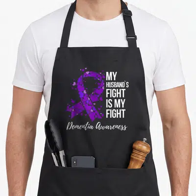 Dementia husband apron - Purple heart awareness ribbon with My Husband's Fight Is My Fight text and Dementia Awareness — shown on a black cotton canvas apron against a white background