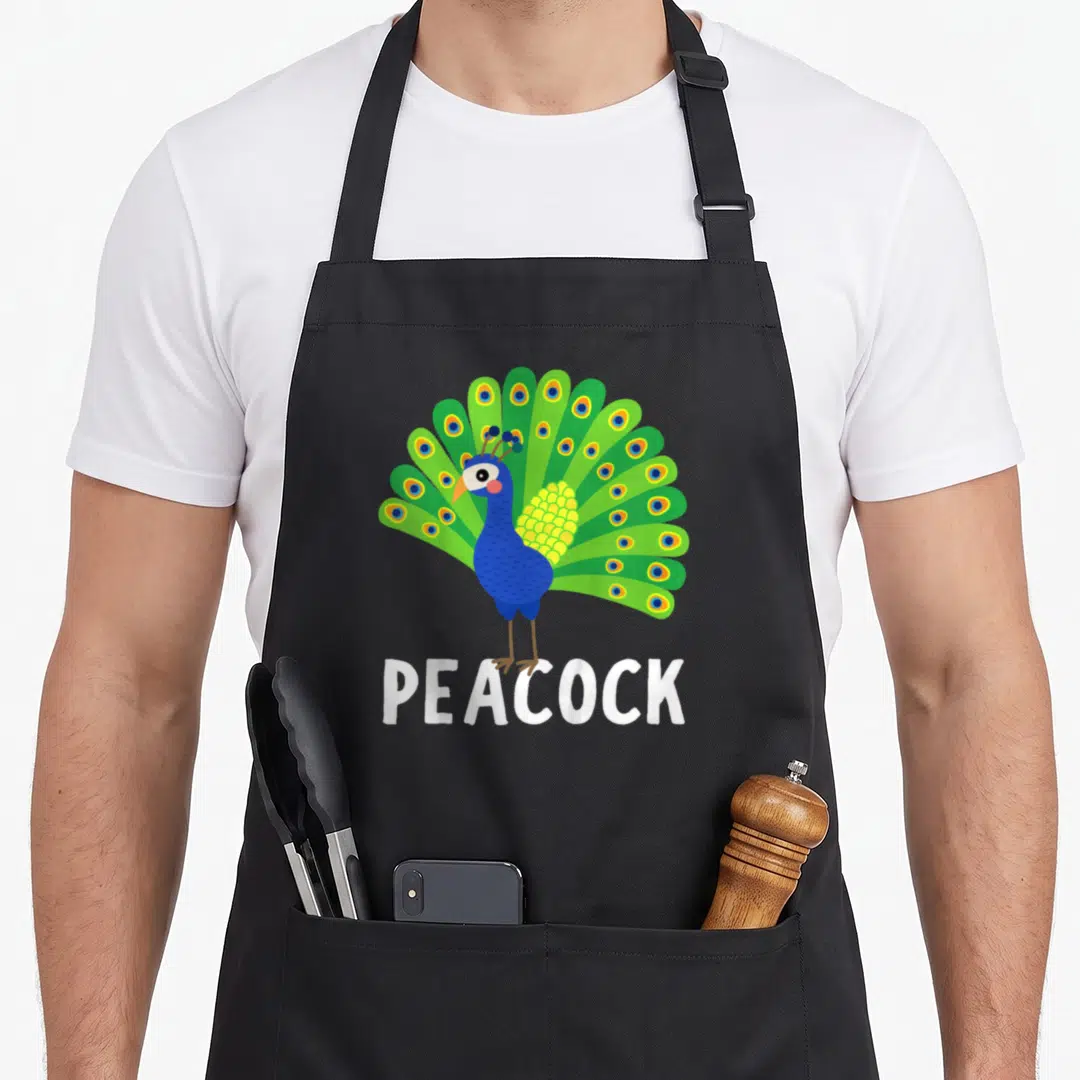 Vintage animal apron for grilling - Cartoon peacock with blue body and fanned green tail above white PEACOCK text — shown on a black cotton canvas apron against a white background