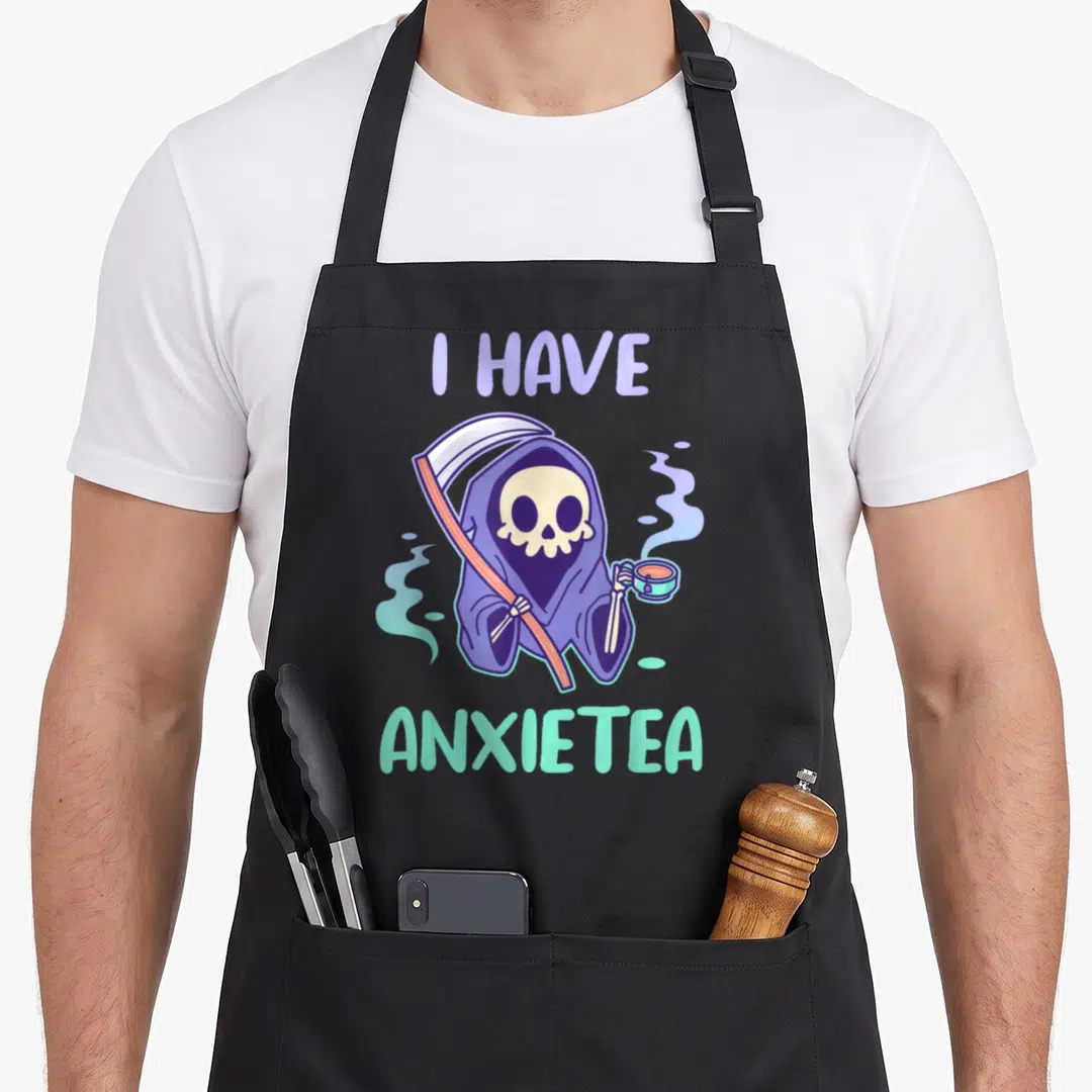 Anxietea tea apron - Cartoon grim reaper holding scythe and tea cup with I HAVE ANXIETEA text — shown on a black cotton canvas apron against a white background
