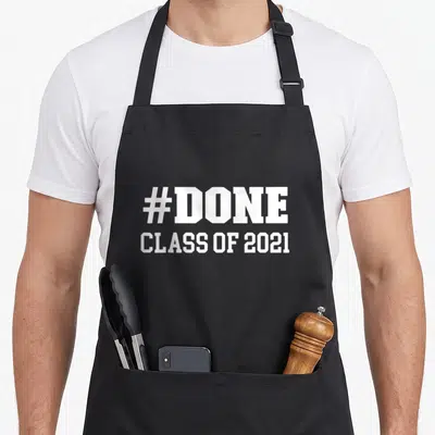 Class congrats apron - White #DONE and CLASS OF 2021 text on grey background — shown on a black cotton canvas apron against a white background