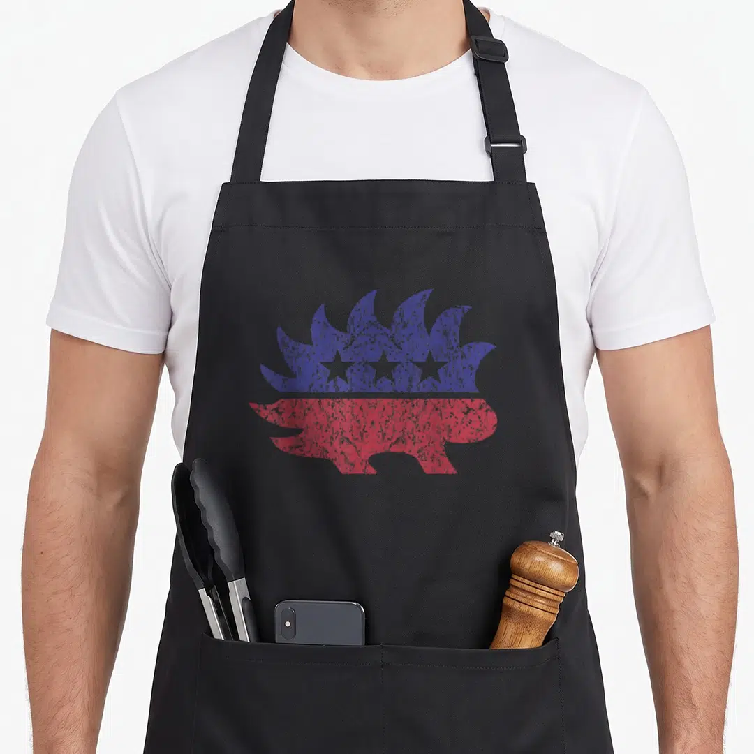 Libertarian distressed apron - Hedgehog silhouette split horizontally into blue top with three white stars and red — shown on a black cotton canvas apron against a white background