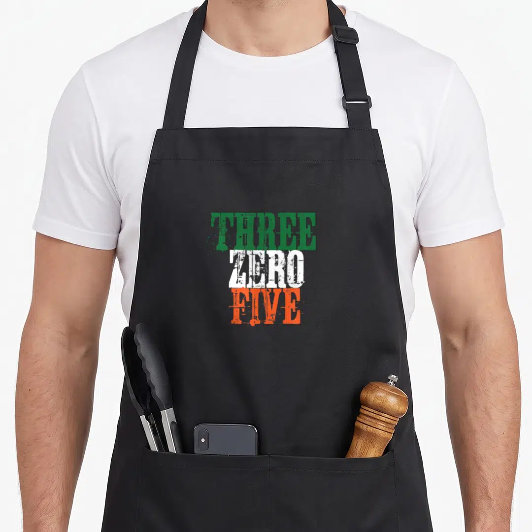 Three miami apron - Stacked typography reading THREE in green, ZERO in white, and FIVE in orange — shown on a black cotton canvas apron against a white background