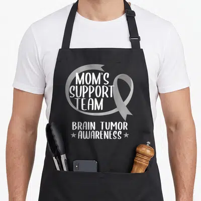 Tumor ribbon apron - Grey ribbon with white Mom's Support Team Brain Tumor Awareness text and two stars — shown on a black cotton canvas apron against a white background