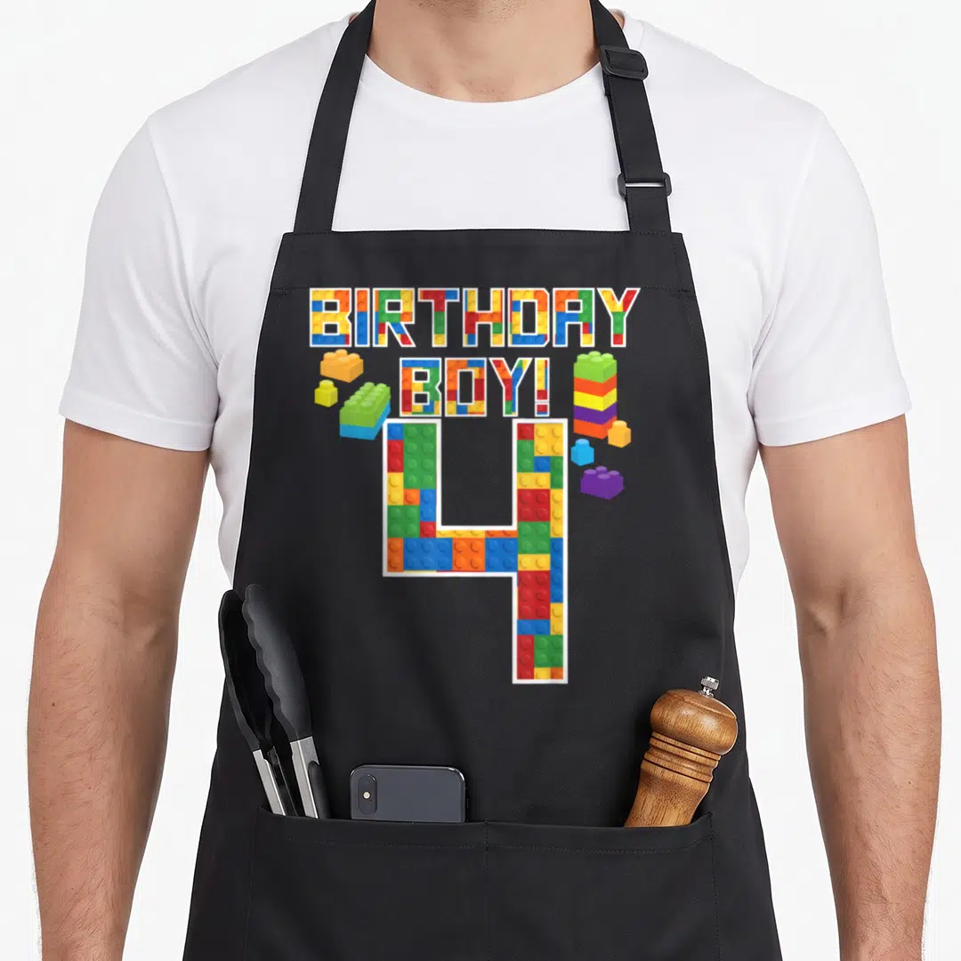 4th building aprons - BIRTHDAY BOY! 4 text and loose bricks in red blue green yellow orange purple — shown on a black cotton canvas apron against a white background