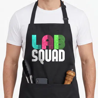 Squad laboratory apron - Stacked LAB SQUAD text in cyan pink green bubbles and white block letters — shown on a black cotton canvas apron against a white background