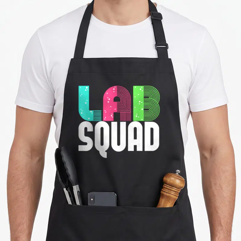Squad laboratory apron - Stacked LAB SQUAD text in cyan pink green bubbles and white block letters — shown on a black cotton canvas apron against a white background