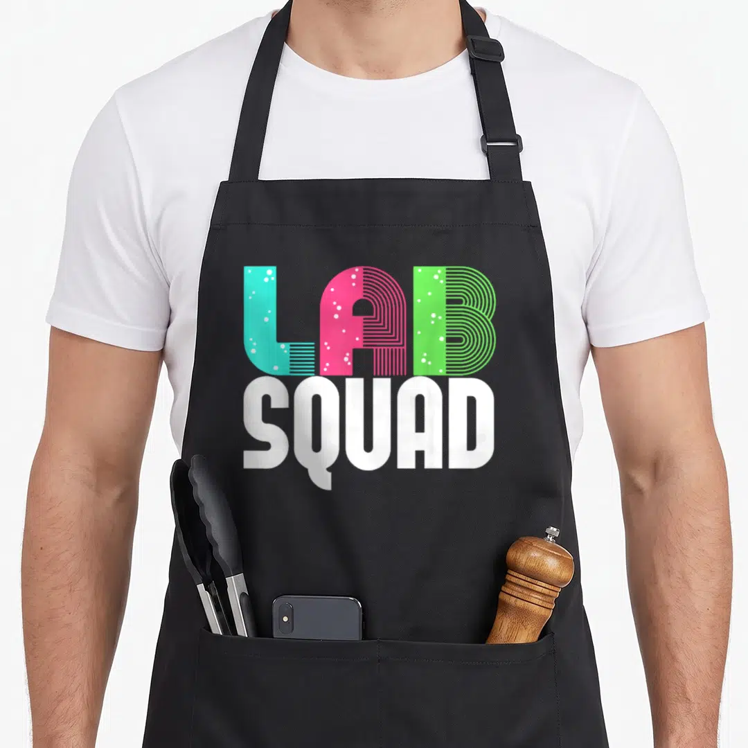 Squad laboratory apron - Stacked LAB SQUAD text in cyan pink green bubbles and white block letters — shown on a black cotton canvas apron against a white background