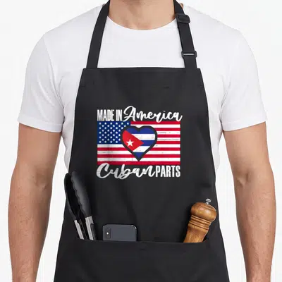 Part american flag apron - Distressed US flag with heart Cuban emblem and text Made in America Cuban Parts — shown on a black cotton canvas apron against a white background