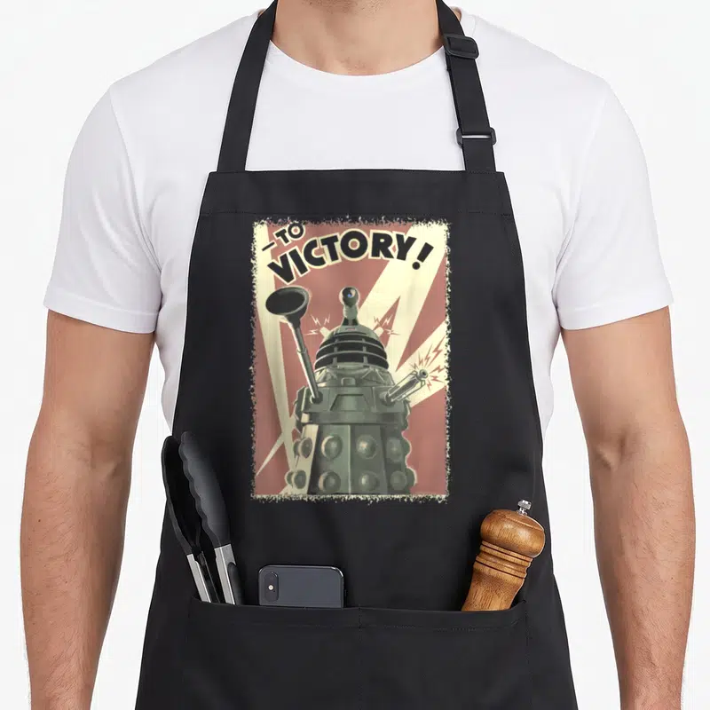 Propoganda doctor apron - Retro Dalek poster with -TO VICTORY! text on red and cream rays — shown on a black cotton canvas apron against a white background