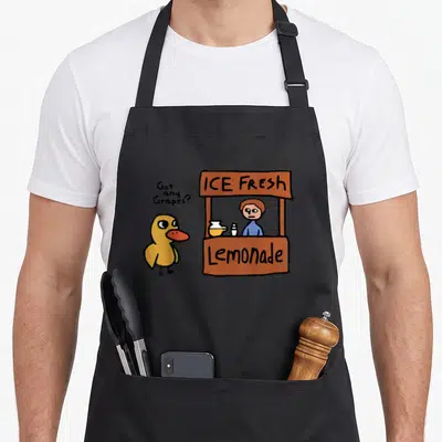 Vintage grape duck apron - Cartoon yellow duck asking Got any Grapes near a brown lemonade stand with blue shirt person — shown on a black cotton canvas apron against a white background