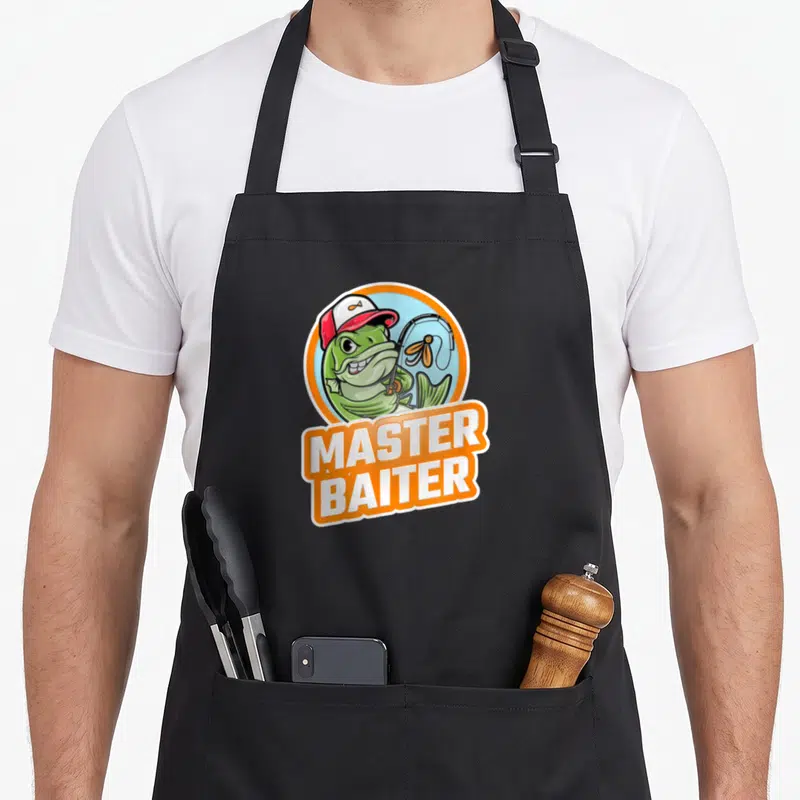 Bass master apron - Cartoon green fish in red cap holding rod above white MASTER BAITER text in orange banner — shown on a black cotton canvas apron against a white background