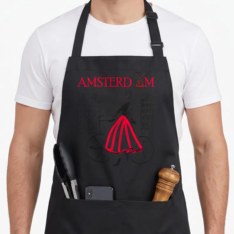 Funny amsterdam bicycle apron - Red AMSTERDAM text with windmill, woman in red skirt next to bicycle and buildings — shown on a black cotton canvas apron against a white background