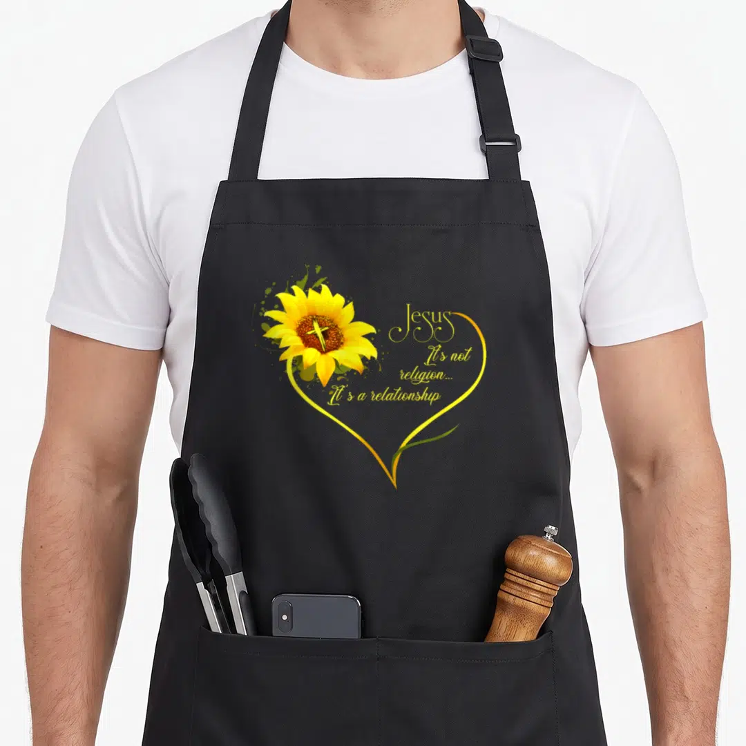 Jesus sunflower apron - Sunflower with cross and yellow heart enclosing text about Jesus and relationship — shown on a black cotton canvas apron against a white background