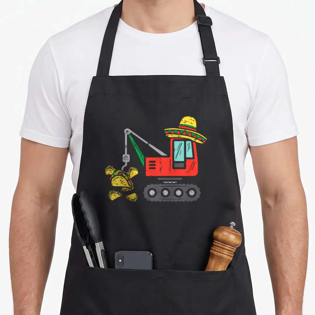 Crane mexican apron - Red excavator wearing yellow sombrero dropping tacos cartoon illustration — shown on a black cotton canvas apron against a white background