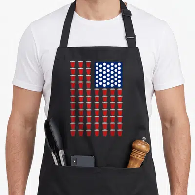 Trendy 4th of july apron - Grid of red cups forming stripes next to white circles on a blue square — shown on a black cotton canvas apron against a white background