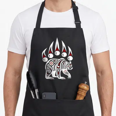 Native pride apron - Stylized white and red bear beneath five vertical claw marks in line art — shown on a black cotton canvas apron against a white background
