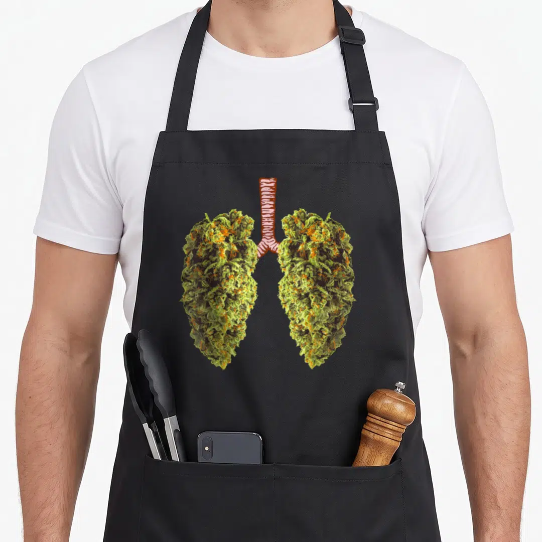 Weed lungs apron - Two green and orange cannabis buds arranged as lungs with a red and white striped trachea connector — shown on a black cotton canvas apron against a white background