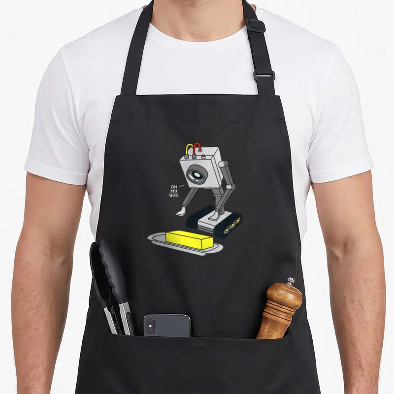Pass butter apron - Grey robot looking at yellow butter block with white pixel text OH MY GOD — shown on a black cotton canvas apron against a white background