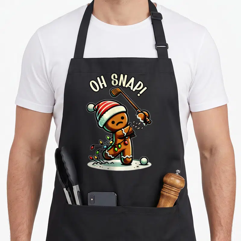 Pajamas gingerbread apron - Arched OH SNAP text above a brown gingerbread man hit by a golf club with Christmas lights — shown on a black cotton canvas apron against a white background