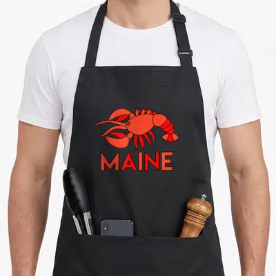 Maine stained apron - Red cartoon lobster graphic above red MAINE text with black outlines — shown on a black cotton canvas apron against a white background