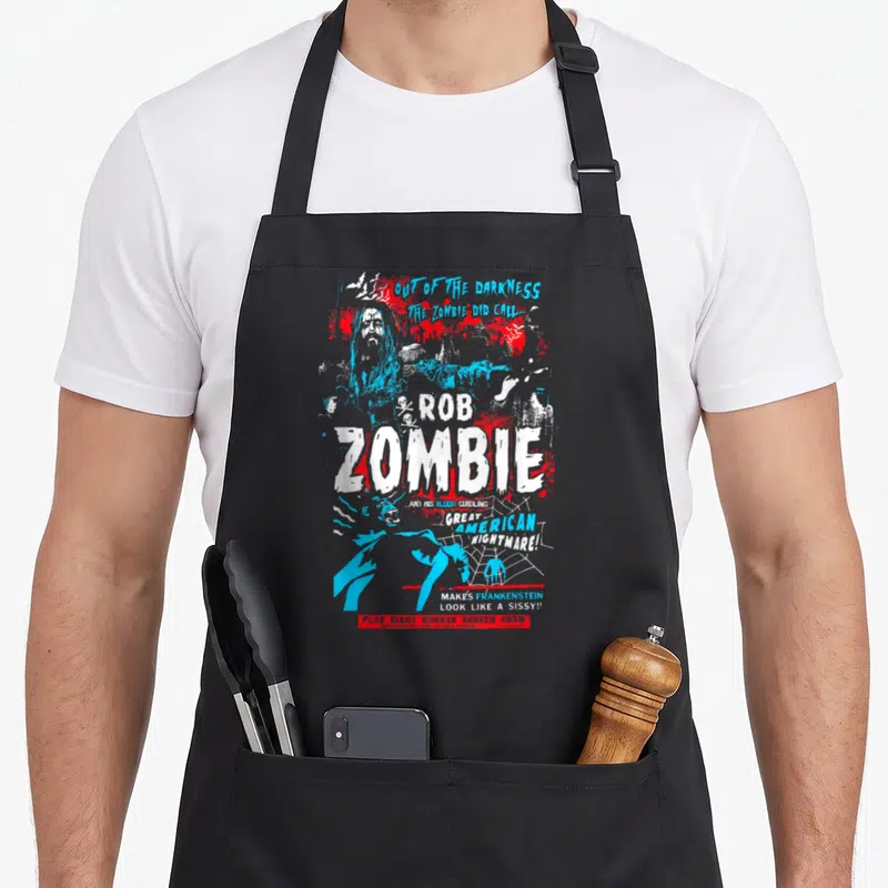 Rob zombie vibes apron - Distressed Rob Zombie poster with blood splatters, spider web, and horror show text in blue — shown on a black cotton canvas apron against a white background