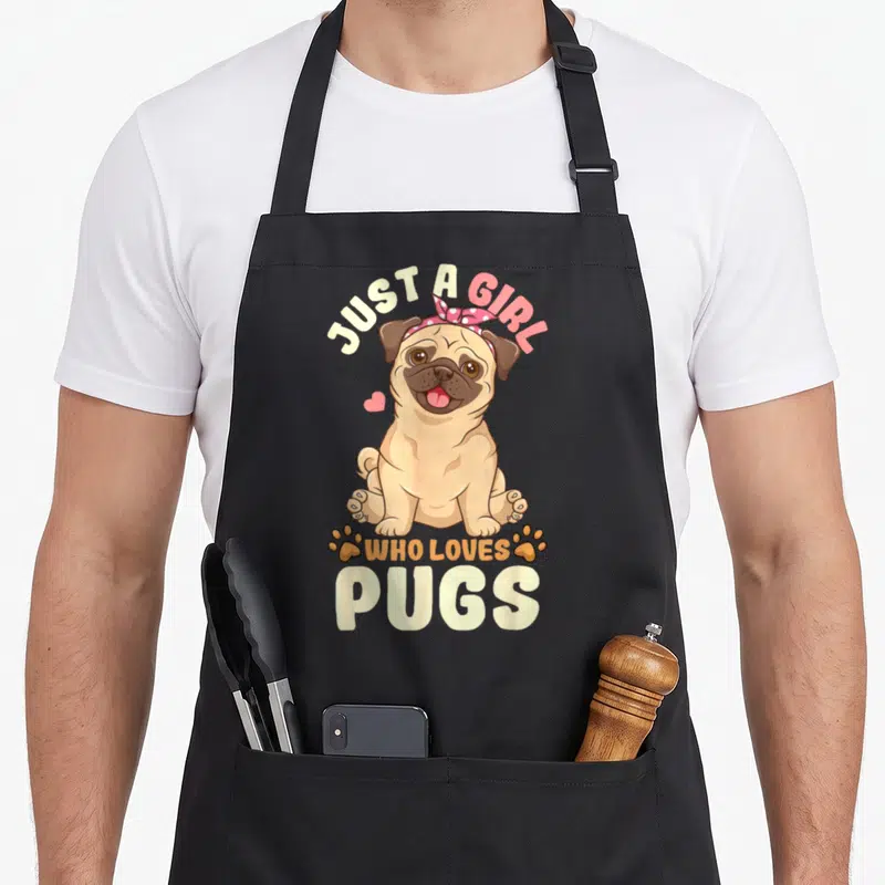 Cute pug dog lover apron - Cartoon pug sitting with bandana, text JUST A GIRL WHO LOVES PUGS and two paw prints — shown on a black cotton canvas apron against a white background