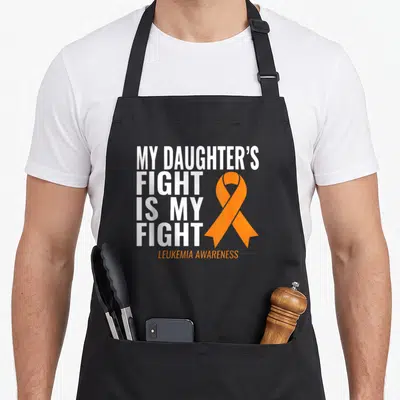 Daughter leukemia awareness apron - White stacked text MY DAUGHTER'S FIGHT IS MY FIGHT beside orange ribbon on black — shown on a black cotton canvas apron against a white background