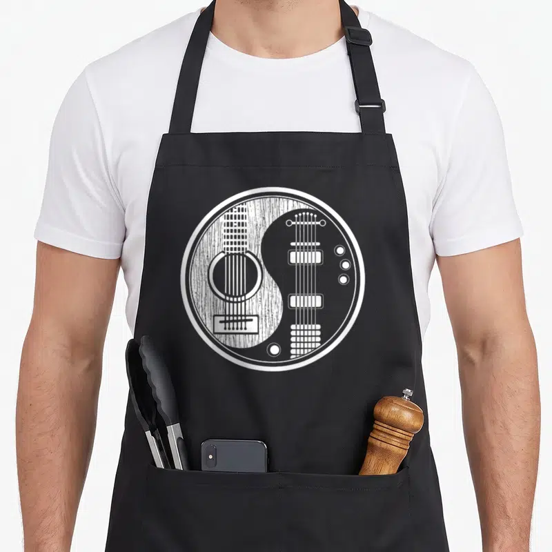 Ying acoustics apron - White line art yin yang formed by acoustic and electric guitar silhouettes on black fabric — shown on a black cotton canvas apron against a white background