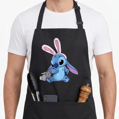 Stitch easter apron - Blue cartoon character wearing pink bunny ears next to a small grey rabbit — shown on a black cotton canvas apron against a white background