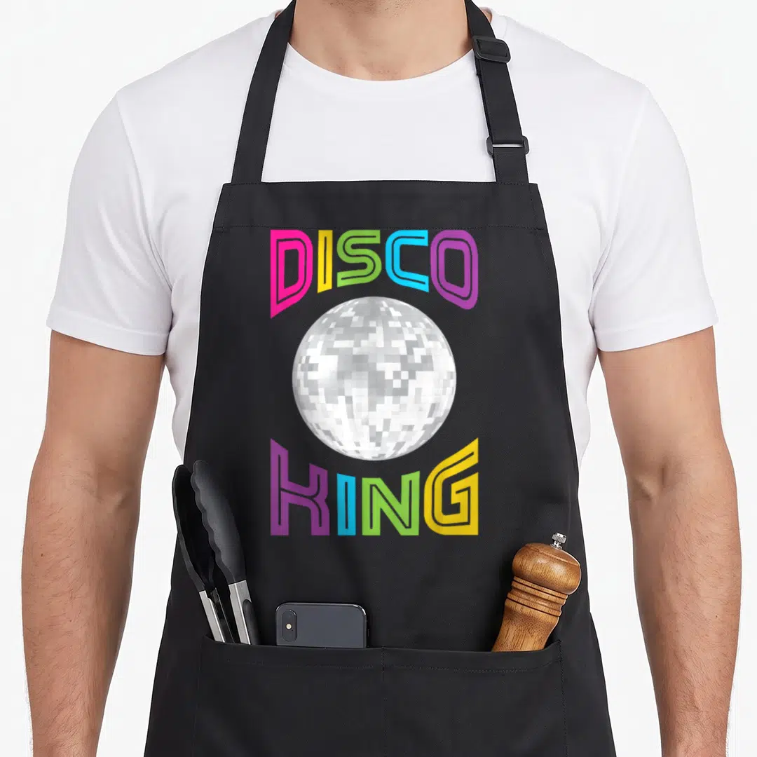 Nostalgia king apron - silver disco ball between arched DISCO and KING text in pink, yellow, green, blue, purple — shown on a black cotton canvas apron against a white background