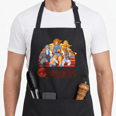 Sunset thunderstorm apron - Four ThunderCats characters grouped before red and orange striped semi-circle sun with logo — shown on a black cotton canvas apron against a white background