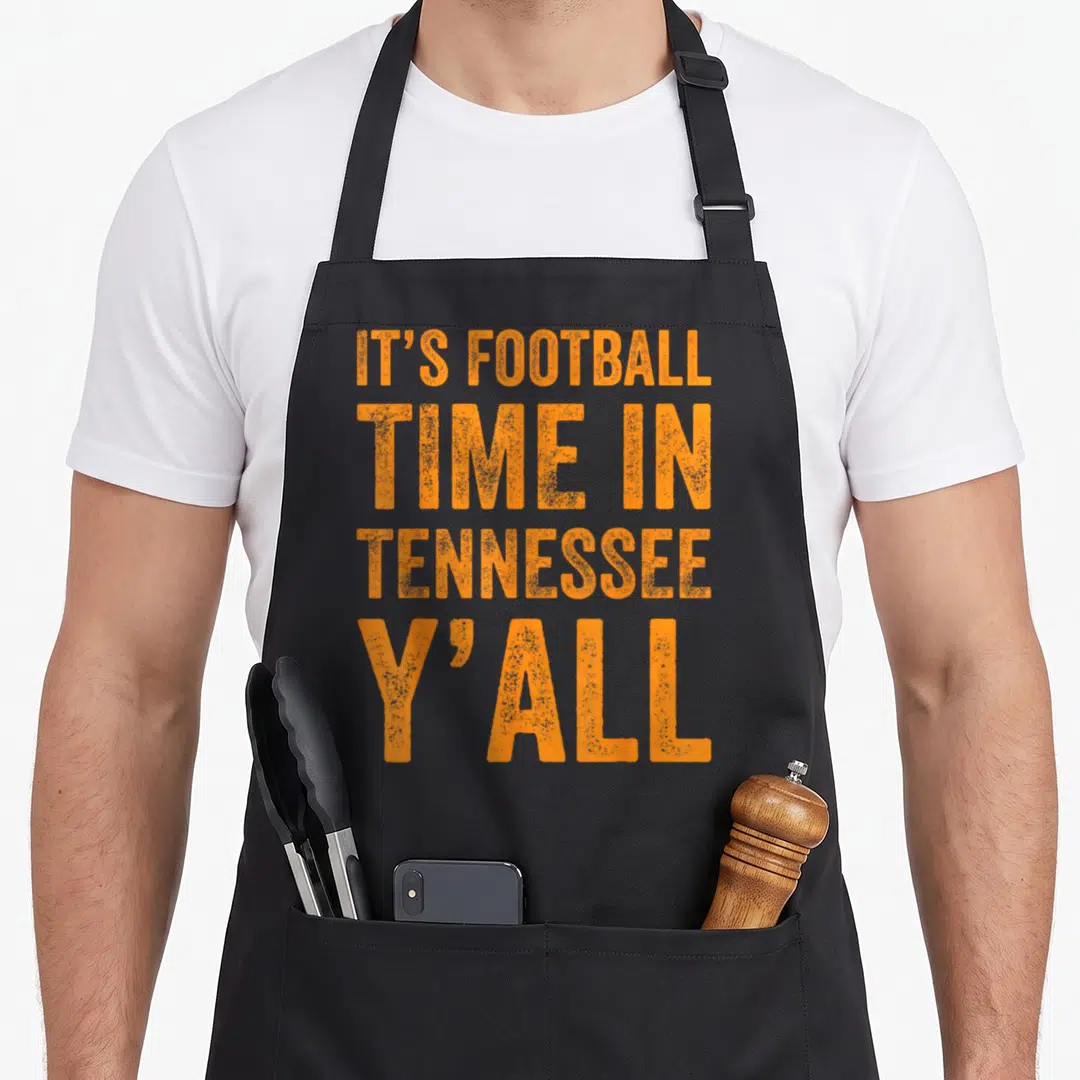 Yall football apron - Orange stacked text IT'S FOOTBALL TIME IN TENNESSEE Y'ALL on grey background — shown on a black cotton canvas apron against a white background