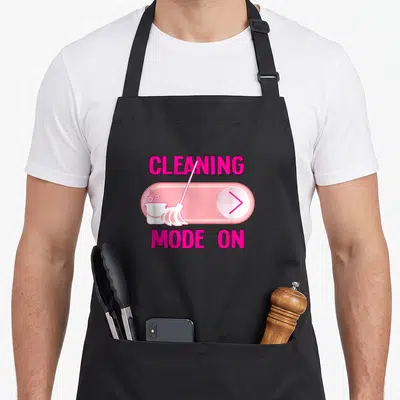 Mode housekeeper apron - Pink toggle switch graphic with broom, bucket, and CLEANING MODE ON text — shown on a black cotton canvas apron against a white background